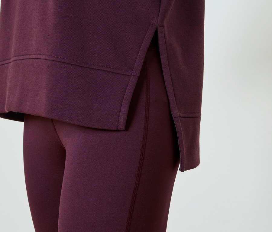Nahaufnahme eines dunkelroten zweiteiligen Trainingsanzugs, bestehend aus Leggings und einem langärmeligen Oberteil mit seitlichem Schlitz.