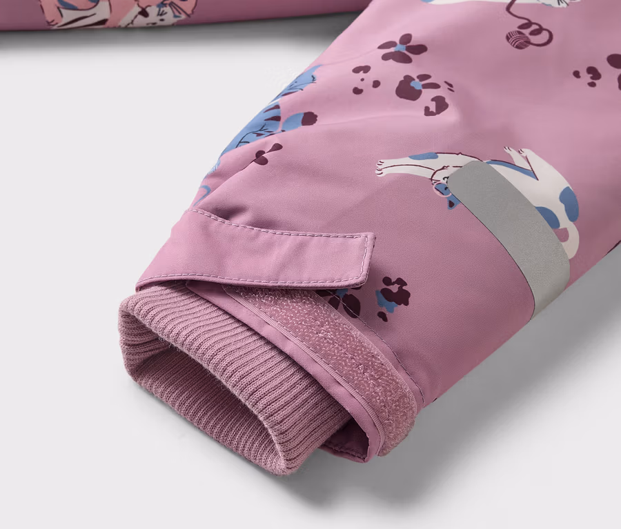 Nahaufnahme des Ärmels einer lila Jacke mit Katzenmuster, geripptem Bündchen, Klettverschluss und reflektierendem Streifen.