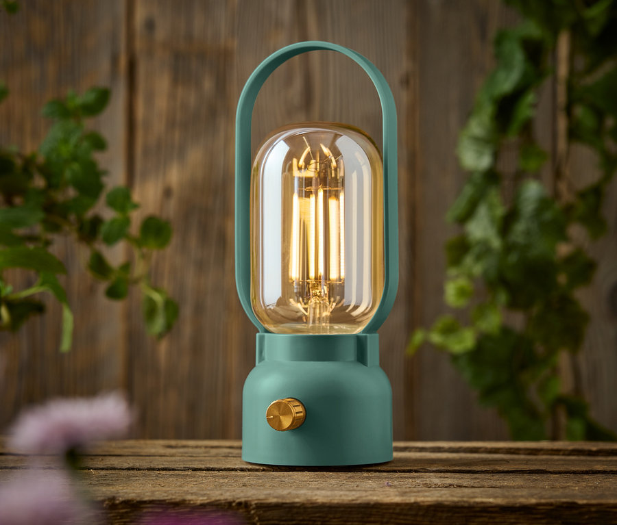 Eine grüne Lampe mit einem goldenen Knopf steht auf einem Holztisch.