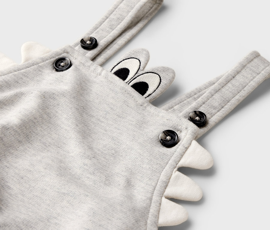 Nahaufnahme eines grauen Baby-Overalls mit Knopfverschluss und Dino-Motiv.
