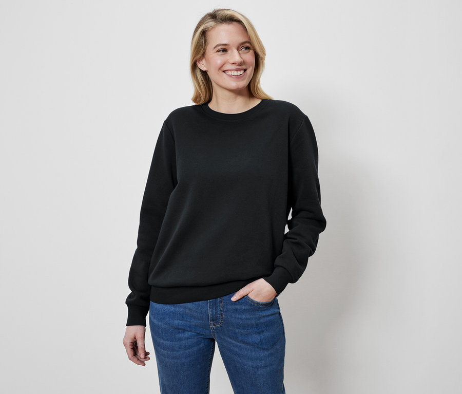 Frau mit blonden Haaren trägt einen schwarzen Pullover und Jeans.