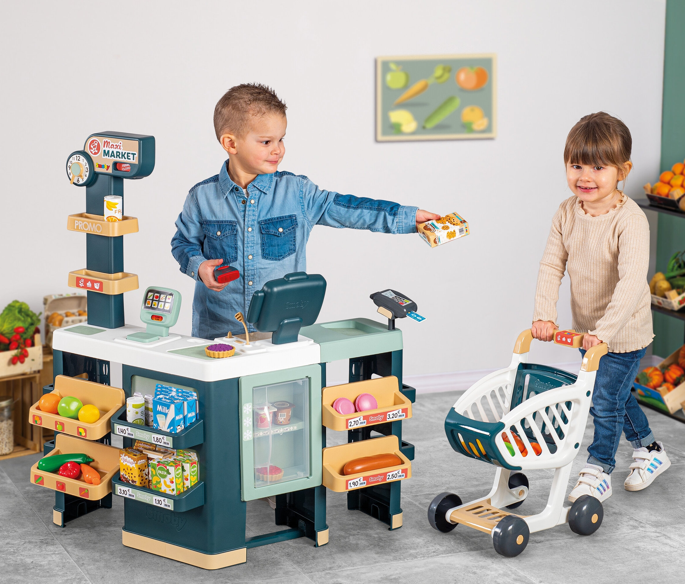 Ein Junge und ein Mädchen spielen mit einem Smoby Supermarkt »Maxi« mit Einkaufswagen. Der Junge hält eine Packung in der Hand, während das Mädchen einen Einkaufswagen schiebt.