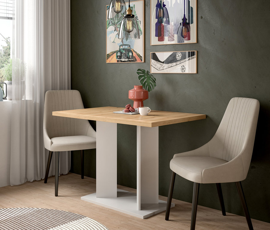 Rechteckiger Holztisch mit weißem Fuß, flankiert von zwei beigen Polsterstühlen mit dunklen Beinen. Auf dem Tisch stehen eine rosa Vase mit Blatt, eine weiße Tasse und rote Macarons. Drei Pendelleuchten hängen darüber, drei gerahmte Bilder schmücken die dunkle Wand. Ein runder gestreifter Teppich liegt auf dem Holzboden.