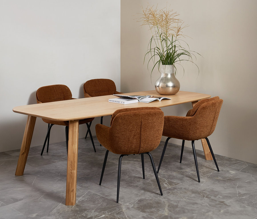 Ein WOOOD Tisch »Tablo« (ca. 180 x 100 cm, naturfarben) mit vier braunen Stühlen. Auf dem Tisch stehen eine silberne Vase mit Ziergras und ein offenes Buch.