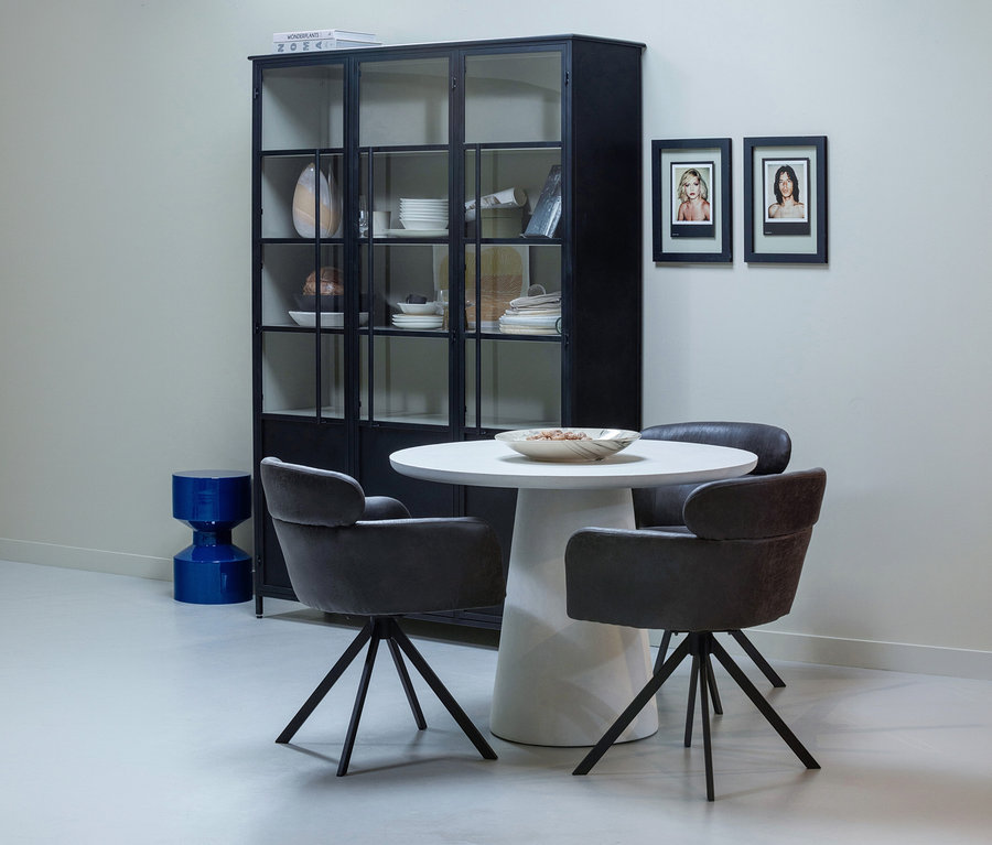 Ein Essbereich mit einem schwarzen Vitrinenschrank, einem runden weißen Tisch mit drei grauen Stühlen und zwei gerahmten Bildern an der Wand.