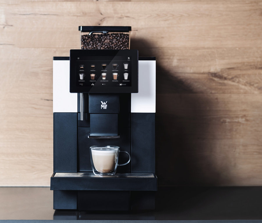 Profi-Kaffeevollautomat »WMF 950 S« vor einer Holzwand. Auf einem Regal darüber befinden sich zwei Blumentöpfe und Tassen.