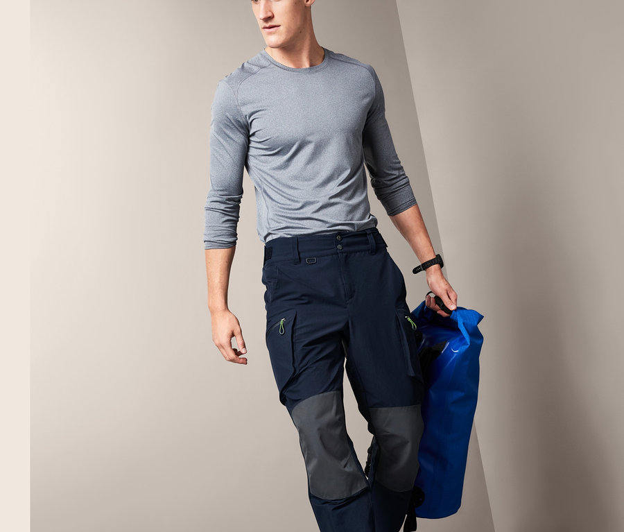 Mann in grauem Shirt und dunkelblauer Segel- und Outdoorhose steigt Stufen hinab und trägt eine blaue Tasche.
