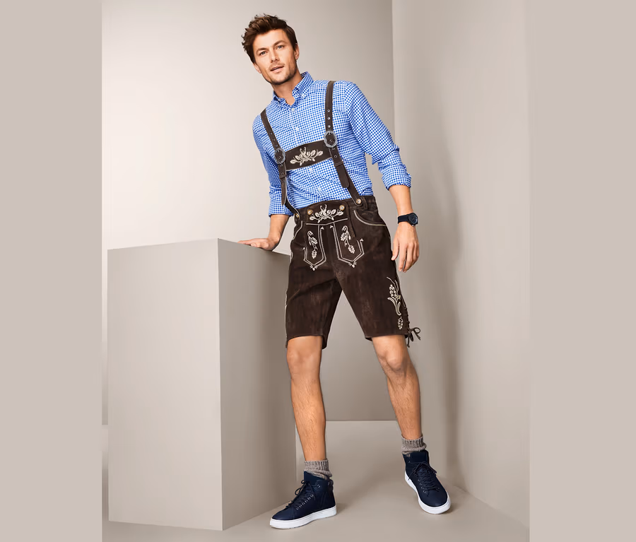 Mann posiert in blauem Hemd und Trachten-Lederhose.