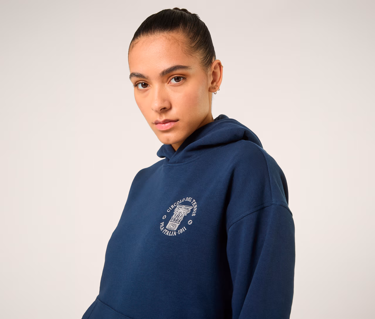 Frau trägt dunkelblauen FILA Damen-Hoodie »MARLIA« mit weißem Logo auf der Brust und blickt in die Kamera.