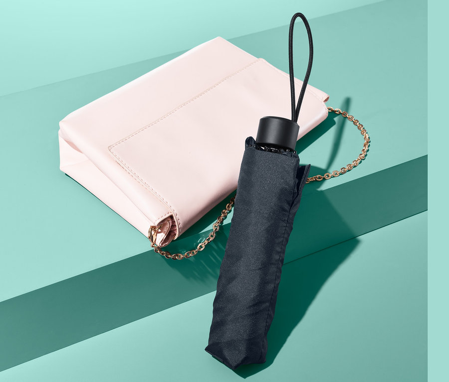 Eine rosa Handtasche mit einem Mini-Regenschirm daneben.