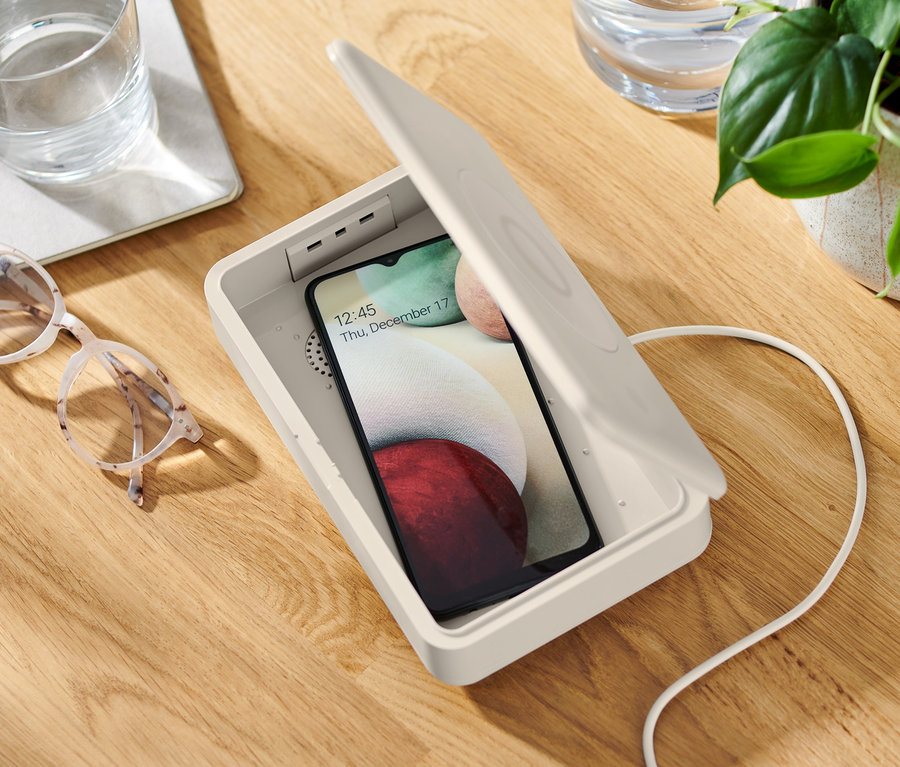 Ein Handy liegt in einer geöffneten UV-Desinfektionsbox mit kabellosem Ladegerät.