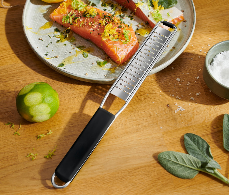 Auf einem Holztisch liegt ein Teller mit Lachs, Zitrone und Limette. Eine Handreibe liegt über den Teller.