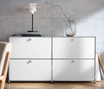 Weißes Sideboard »CN3« mit vier Klappen, darauf eine Tischleuchte aus Metall und eine Vase mit Zweigen.