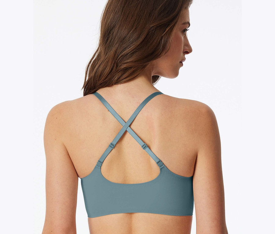 Rückansicht einer Frau mit braunen Haaren, die einen blaugrünen BH mit gekreuzten Trägern trägt.