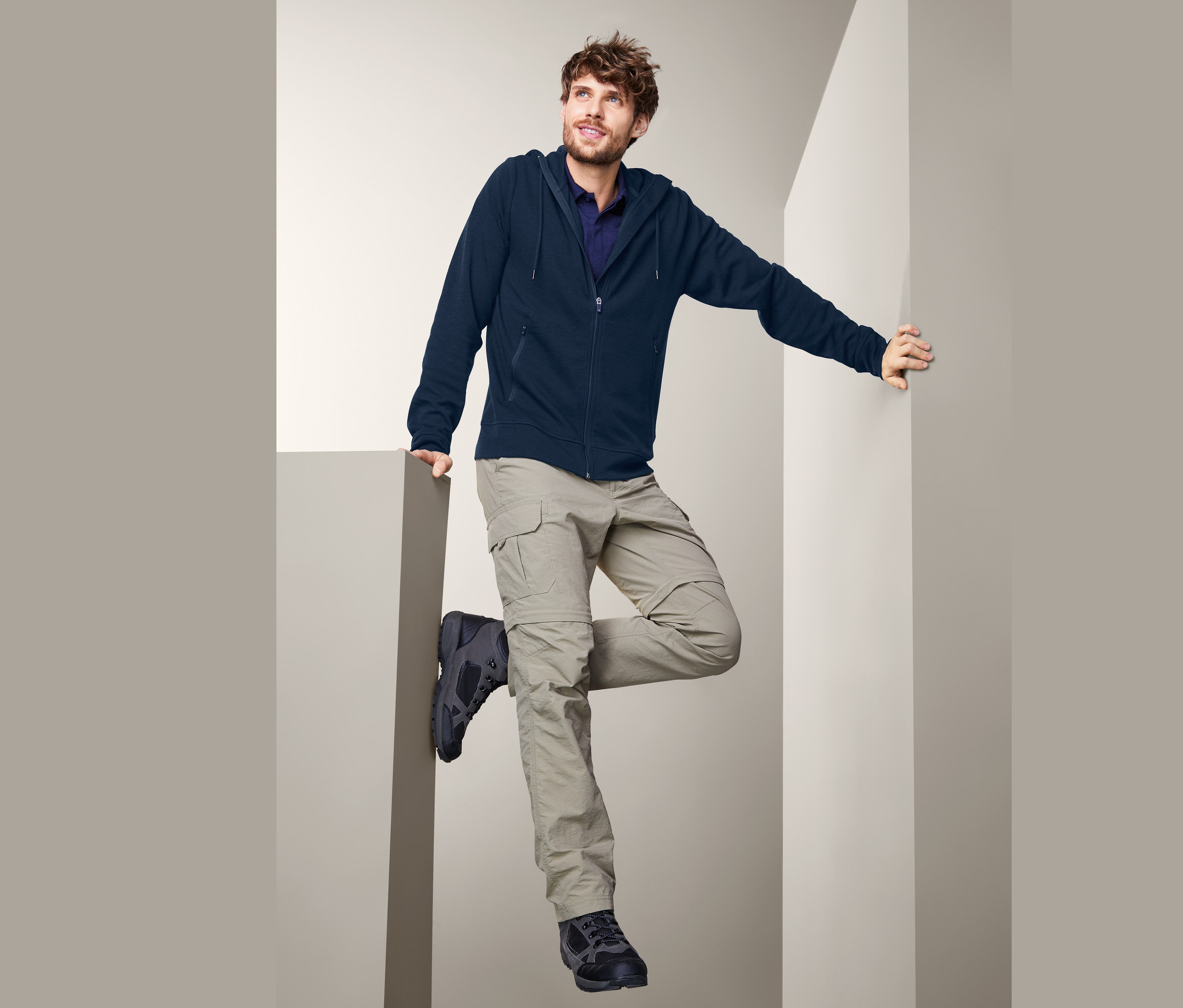 Mann posiert in marineblauer Funktionsjacke mit Merinowolle, beigen Hosen und Trekkingschuhen.