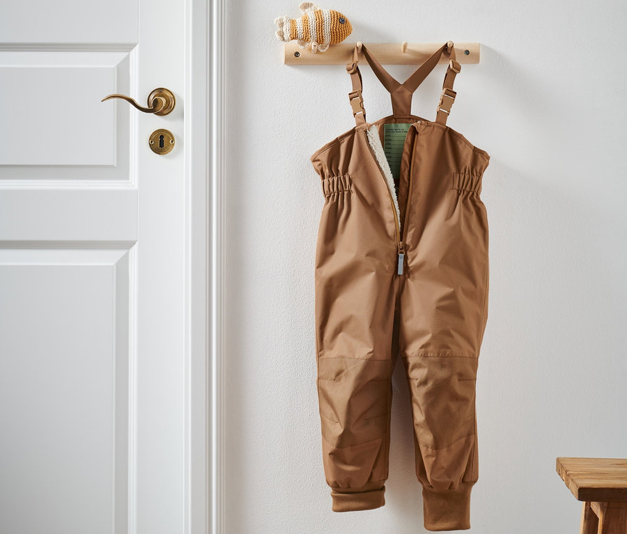 Braune Regenhose hängt an einer Garderobe neben einer weißen Tür.