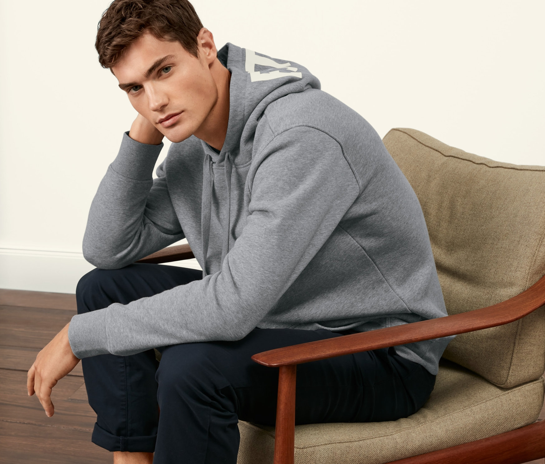 Mann sitzt in einem Sessel und trägt einen grauen Hoodie.