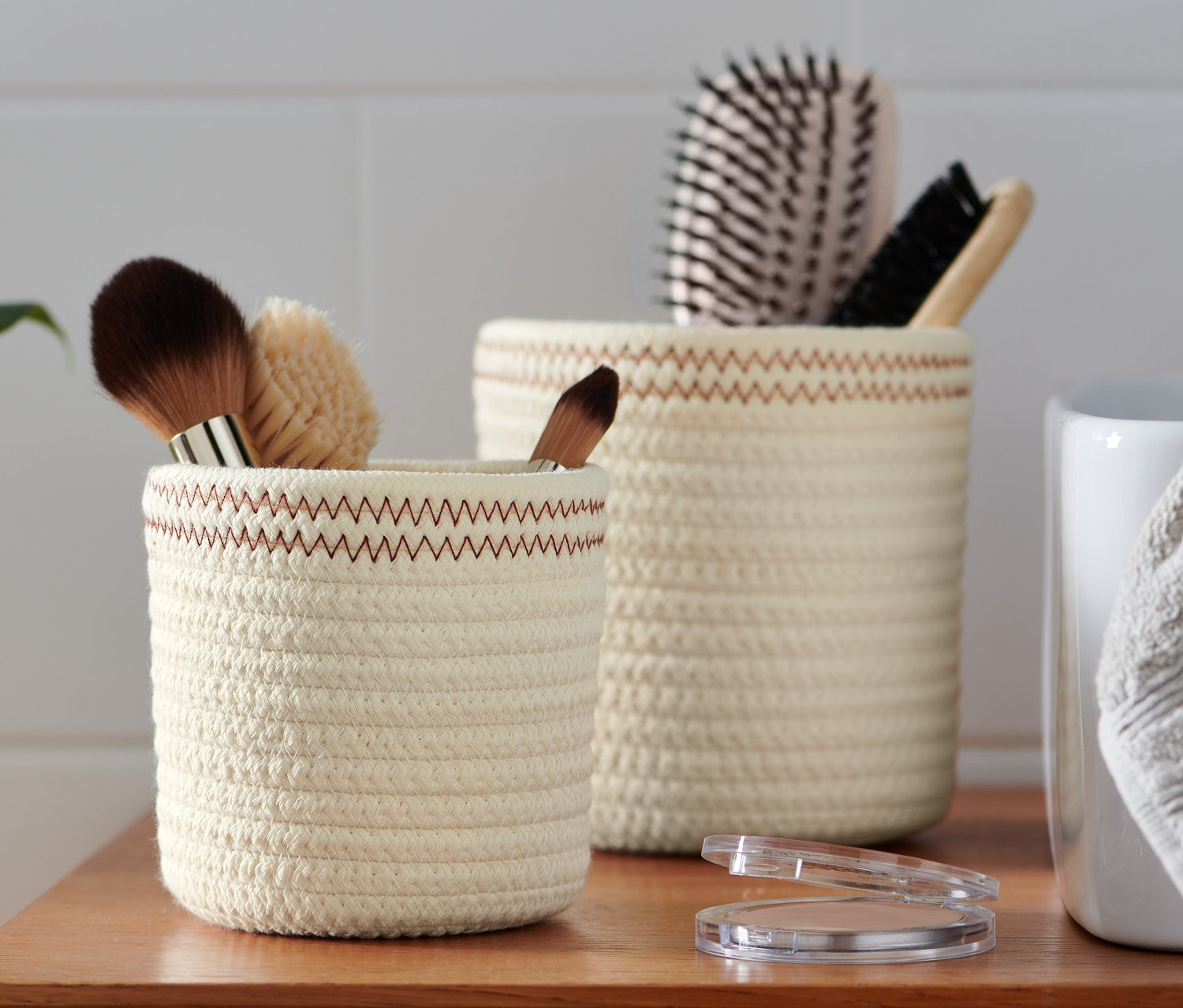 Zwei crèmeweiß-rostfarbene Aufbewahrungskörbe stehen auf einem Holzschrank, einer mit Make-up-Pinseln und der andere mit Haarbürsten.