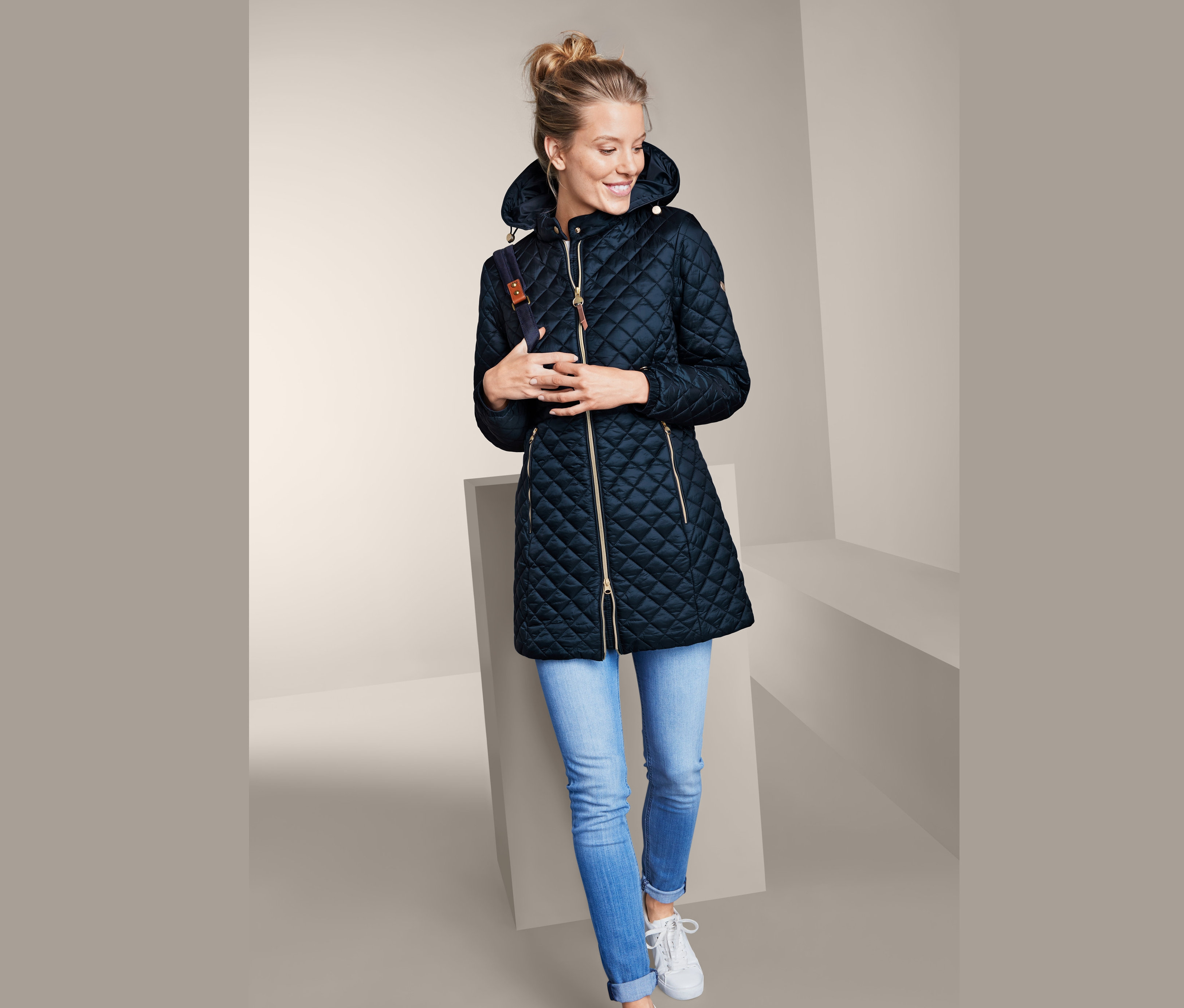 Frau trägt Steppmantel mit Kapuze, Jeans und Turnschuhe.