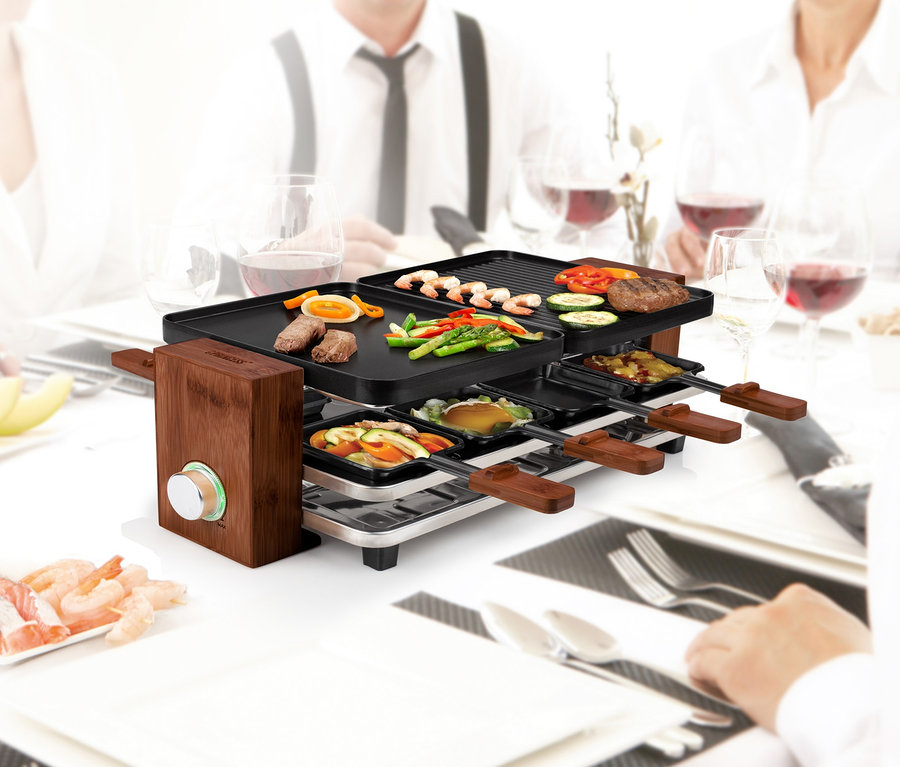 Leute sitzen mit einem Raclette für 8 Personen am Tisch und essen.