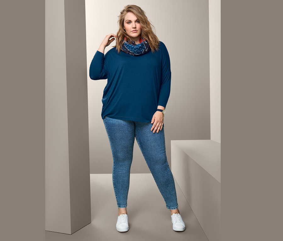 Frau posiert in blauem Oversized-Shirt, Loop-Schal und Treggings.