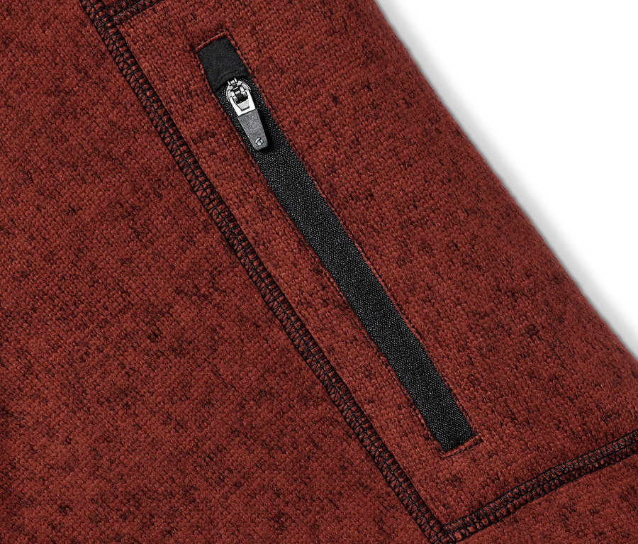 Detailaufnahme eines braunen Strickfleece-Midlayers mit einem schwarzen Reißverschluss an der Tasche.