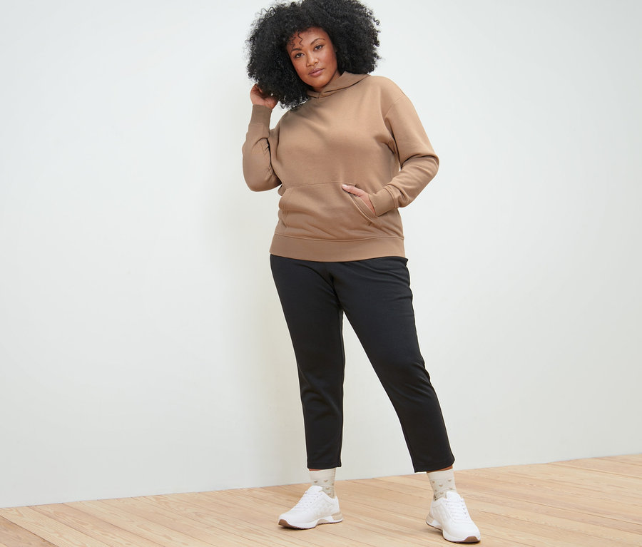 Frau posiert in braunem Hoodie und schwarzen Joggpants.