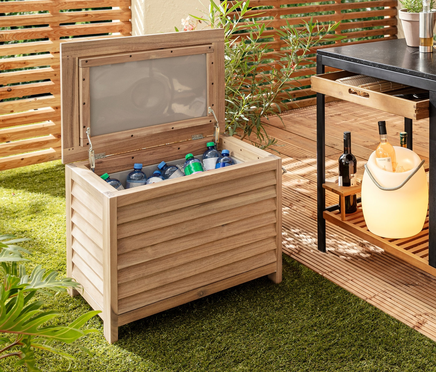 Auf Rasen stehen eine dekorative Coolbox mit Flaschenöffner, daneben ein Grillwagen »Elin« mit Schublade, auf einem Tisch eine LED-Akku-Tischleuchte und ein LED-Flaschenkühler.