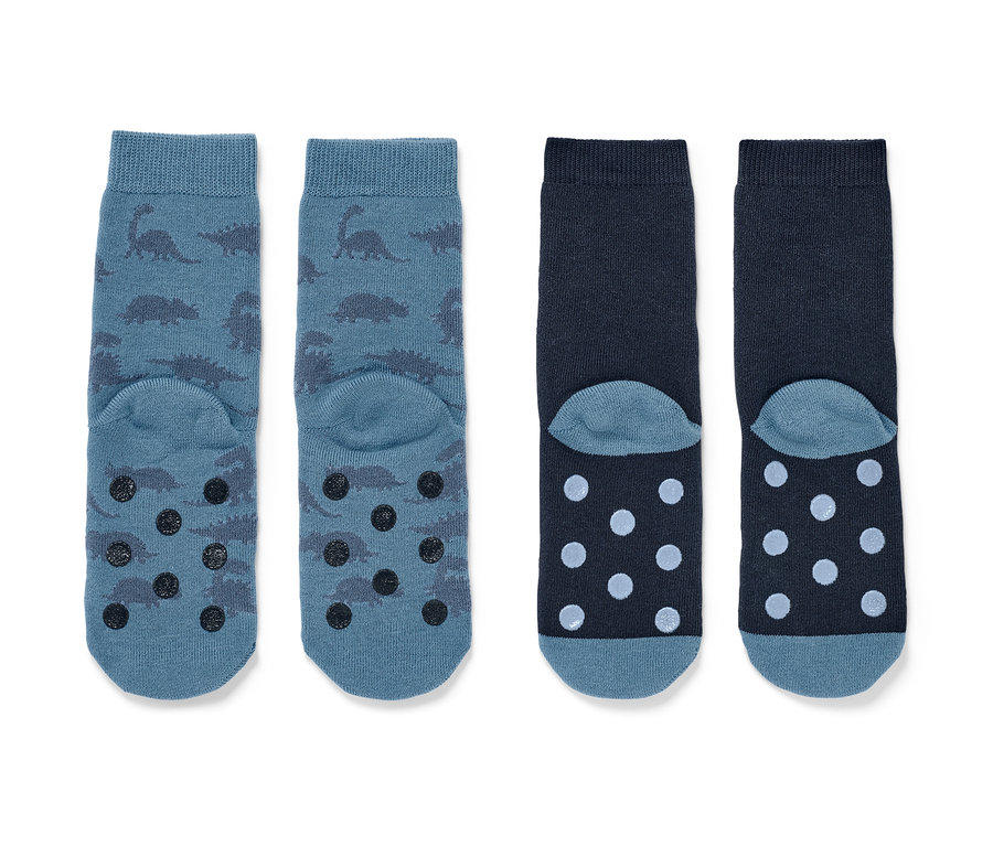 Zwei Paar Kinder-Antirutsch-Socken. Ein Paar blau mit Dinosauriern und Antirutsch-Noppen, das andere dunkelblau mit Punkten.
