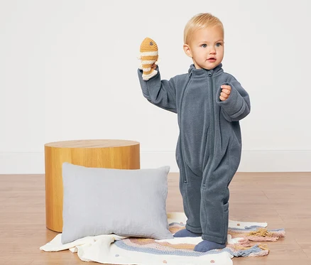 Ein Kleinkind in einem blauen Baby-Fleece-Einteiler hält ein Spielzeug.