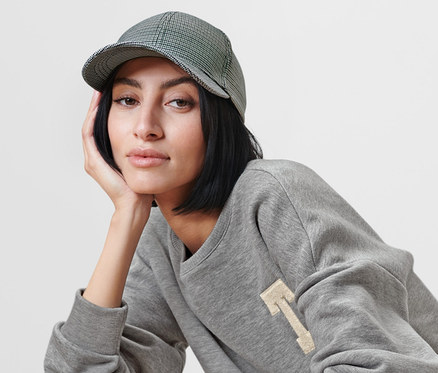 Frau sitzt auf einem Sessel und trägt einen grauen Pullover und eine Kappe.