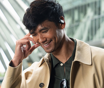 Ein Mann lächelt und berührt einen schwarzen JBL Soundgear Sense Kopfhörer.