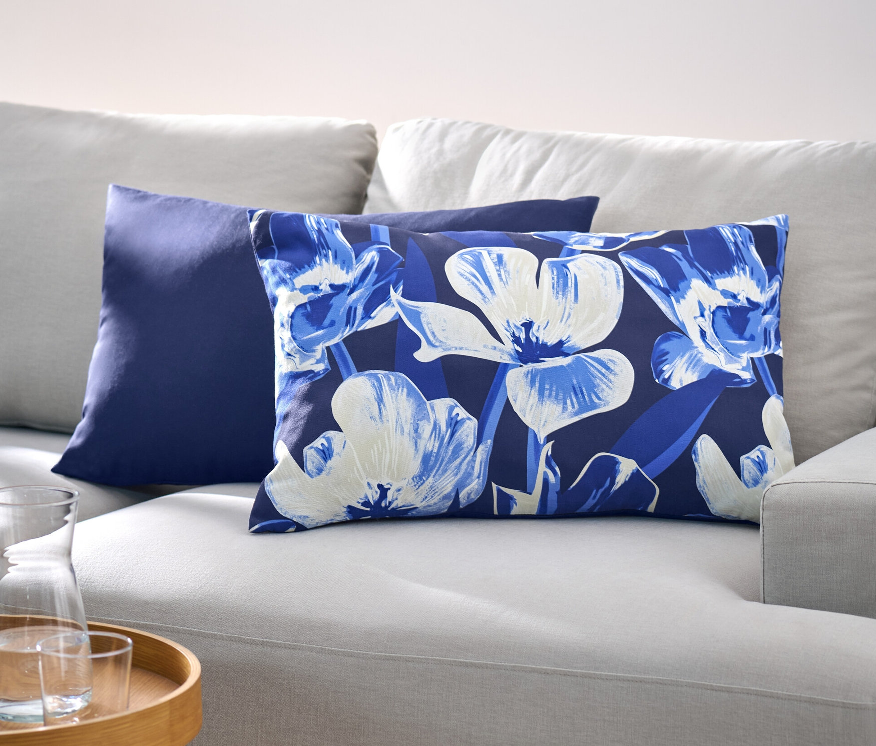 Auf einem hellgrauen Sofa liegen zwei Dekokissen-Bezüge, einer ist dunkelblau, der andere hat ein Blumenmuster.