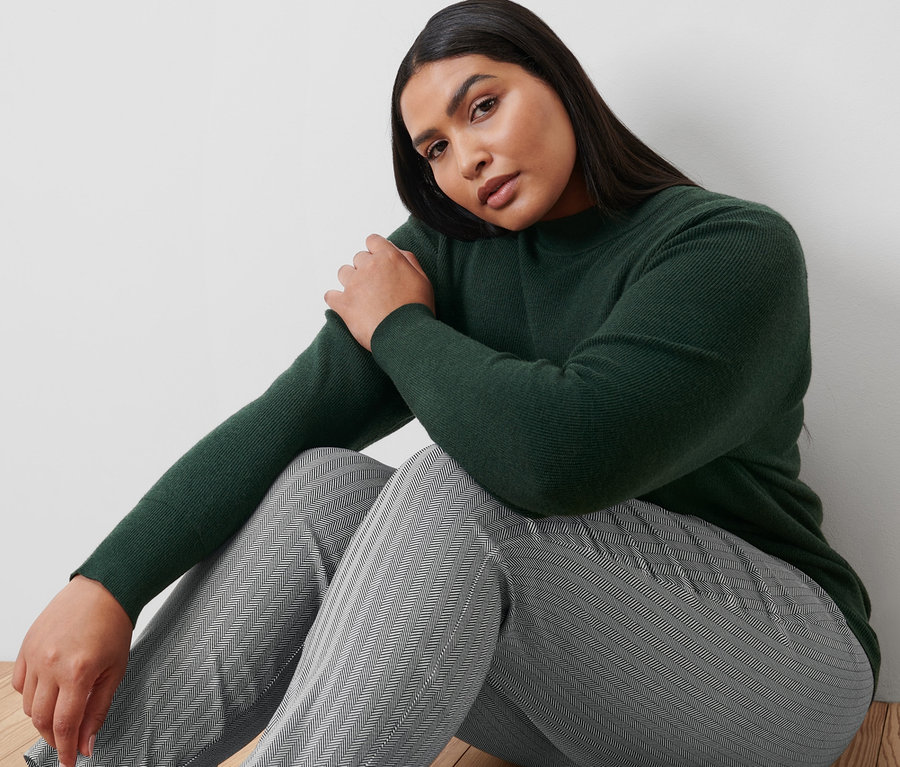 Frau sitzt auf dem Boden und trägt eine bedruckte Stretchhose und einen Feinstrickpullover.