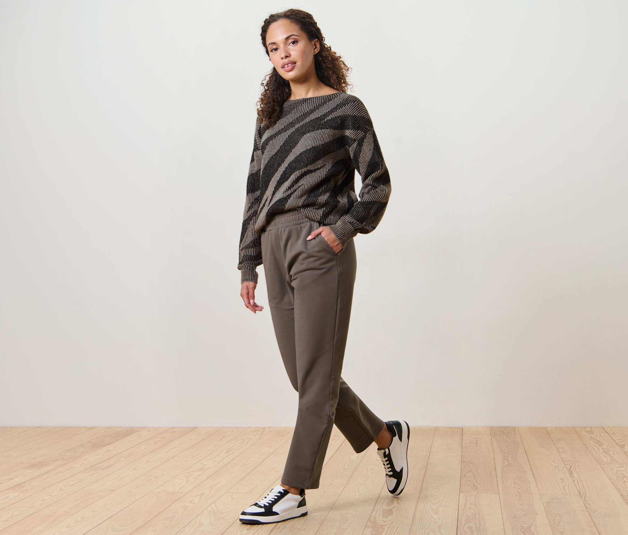 Frau geht, trägt Joggpants und gemusterten Pullover.