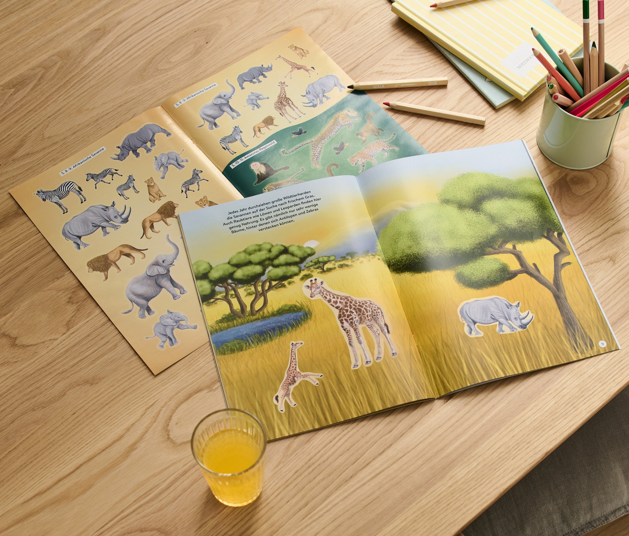 Offenes Stickerbuch "Faszierende Stickerwelt – wilde Tiere" mit Wildtiermotiven auf einem Holztisch.