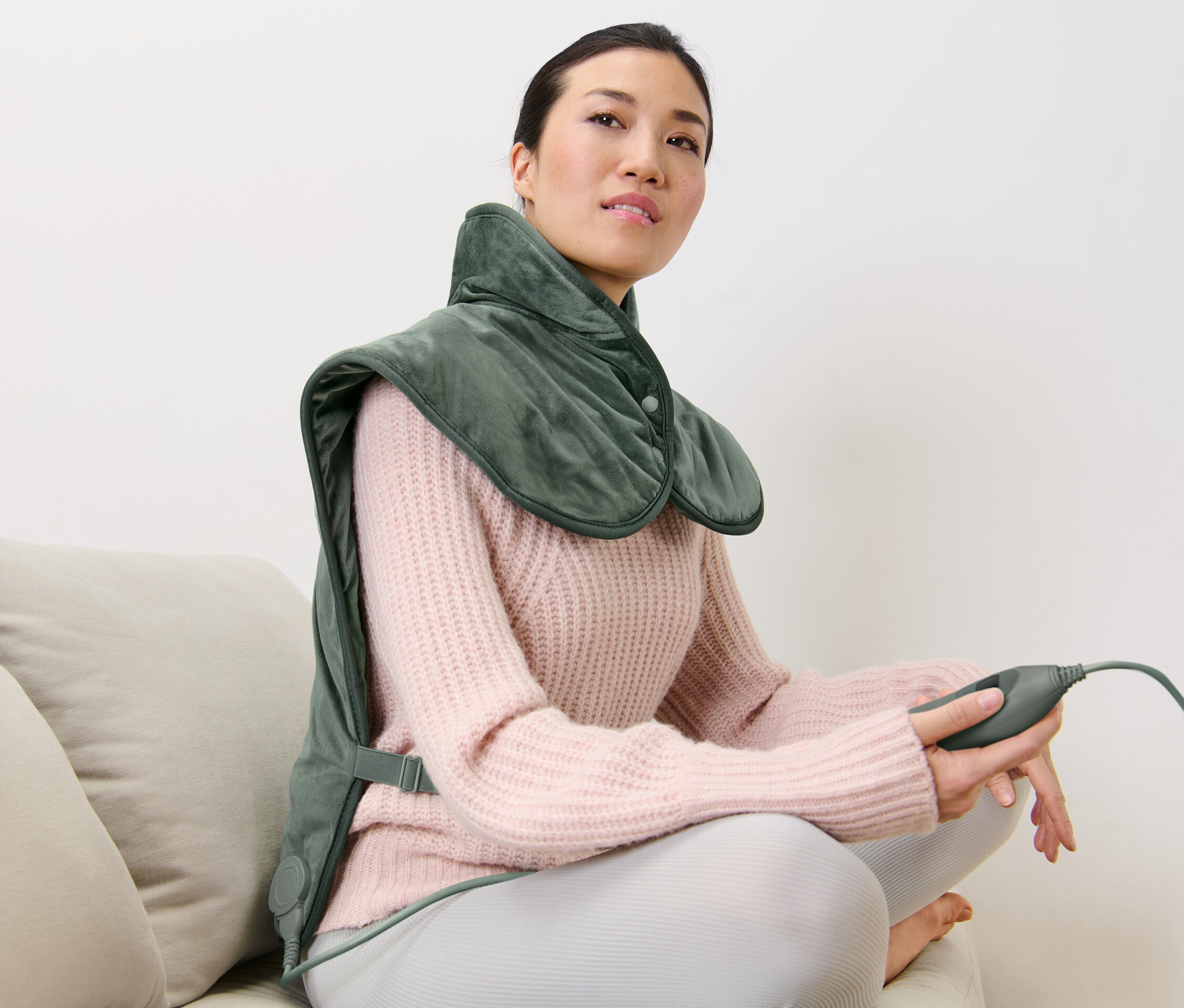 Frau sitzt auf Couch und trägt ein Rückenheizkissen.