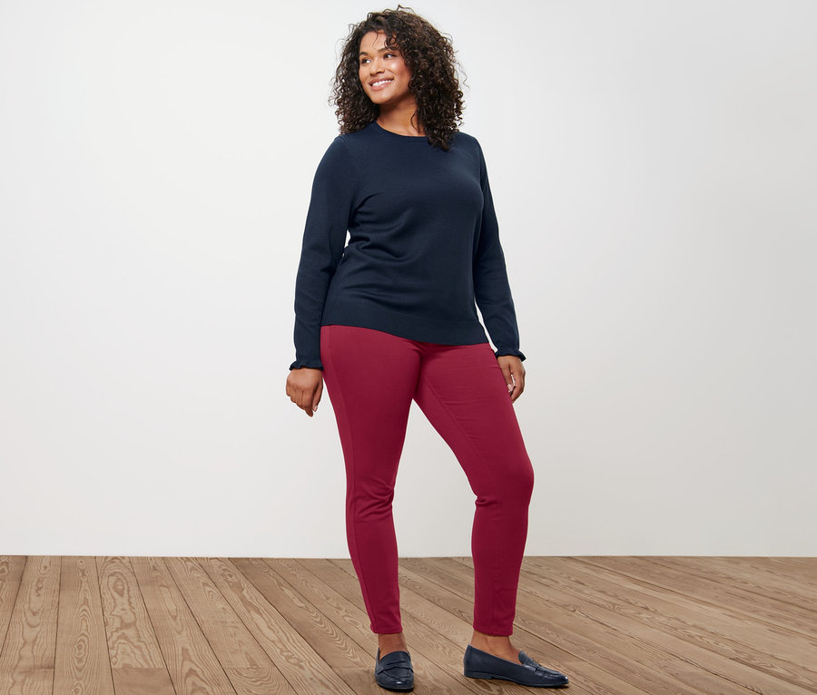 Frau posiert in dunkelblauem Feinstrickpullover mit Rüschendetail und Jeggings.