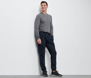 Mann lehnt in grauem Shirt und einer Sweathose an der Wand.