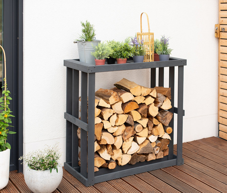Ein »Harald« Kaminholzregal gefüllt mit Holz und Pflanzen steht auf einer Terrasse.