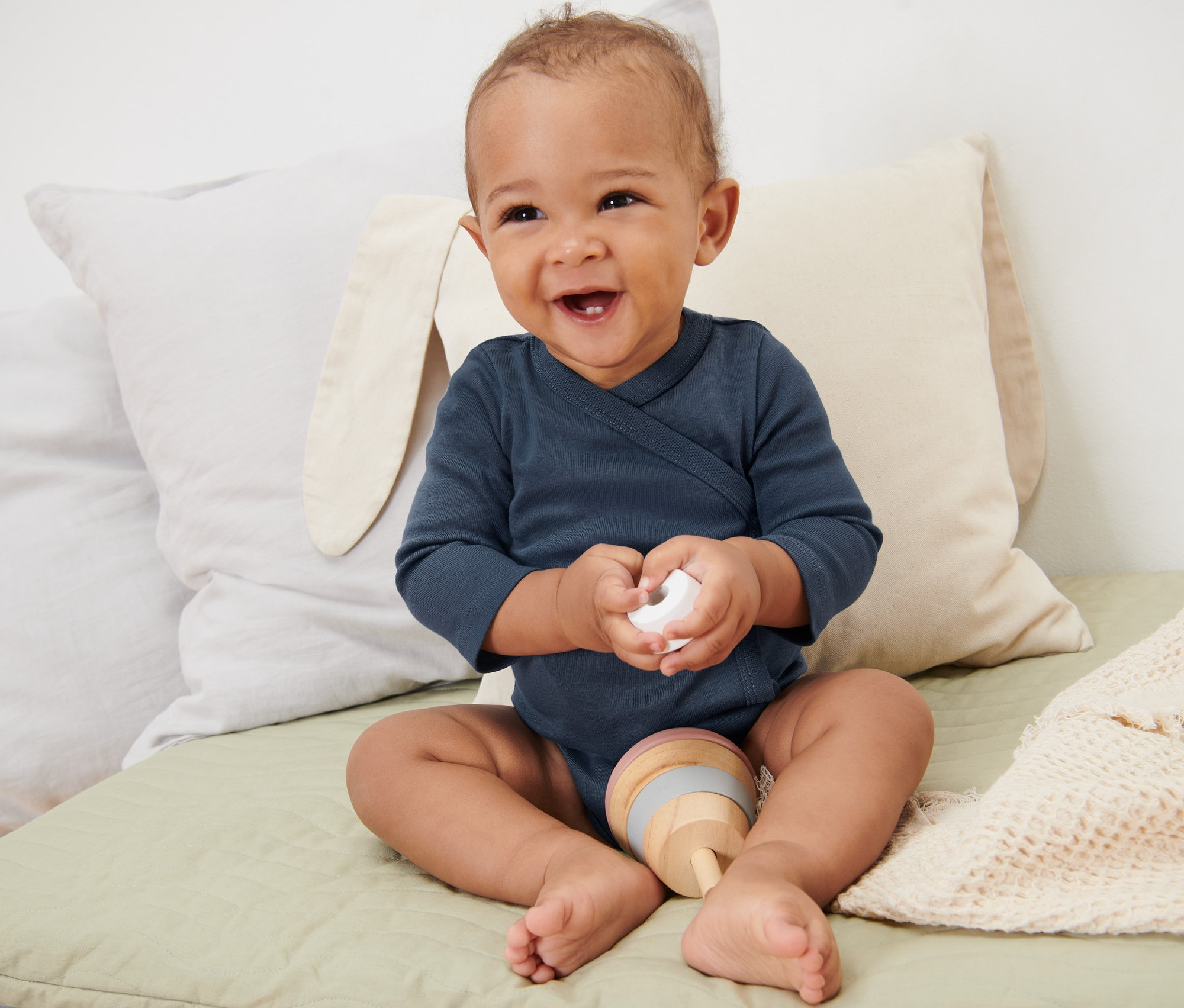 Lächelndes Baby sitzt auf einer Unterlage und trägt einen blauen 5er-Pack Baby-Bodys mit Mitwachsfunktion.