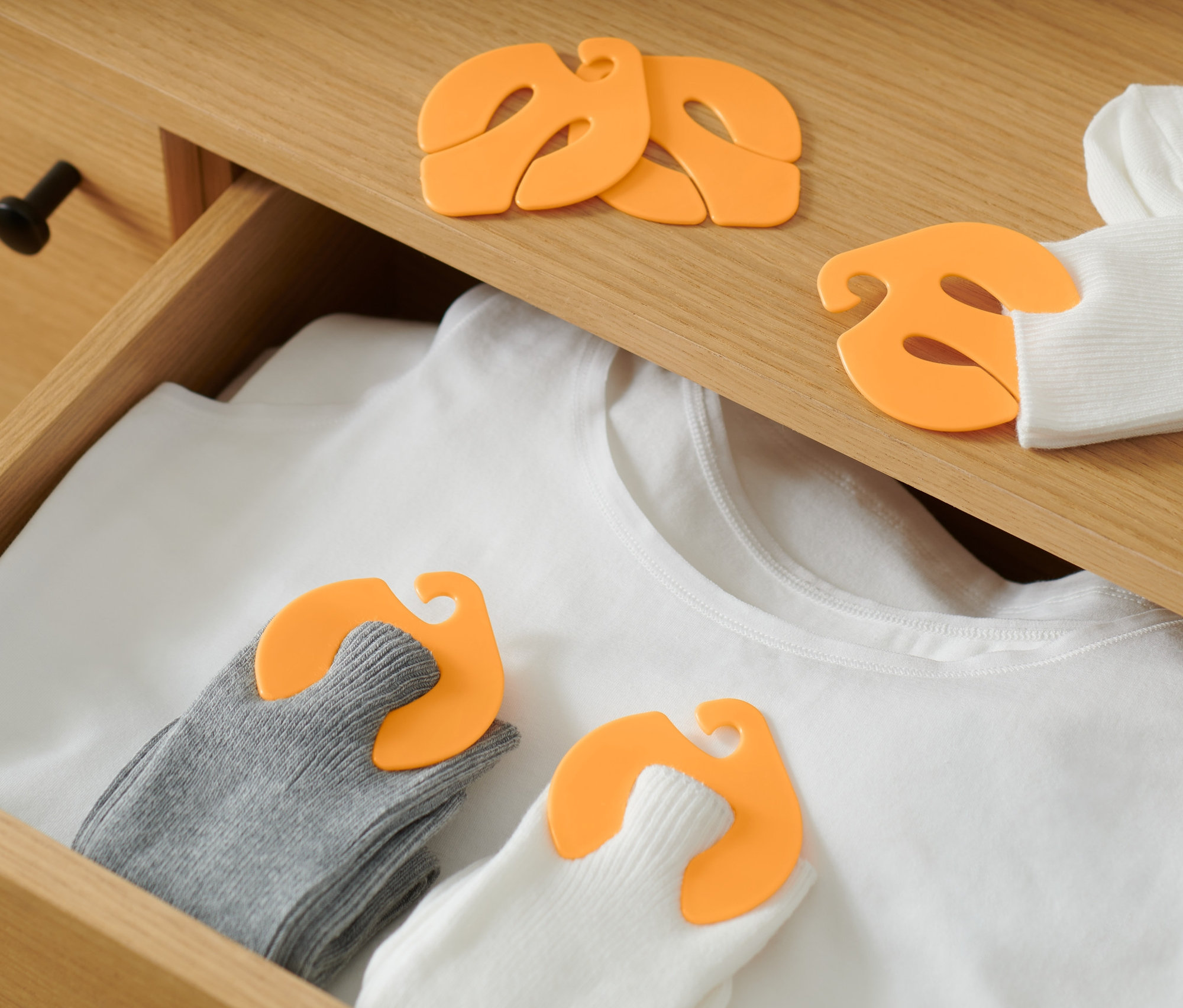 In einer Schublade liegen ein weißes T-Shirt und Socken, die mit 20 Socken-Clips zusammengehalten werden.