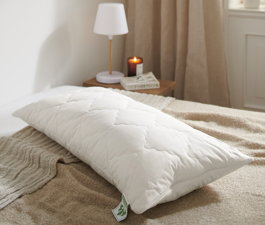 Ein weißes, gestepptes irisette® greenline Kopfkissen mit Lavendel, ca. 80 x 40 cm liegt auf einem Bett.