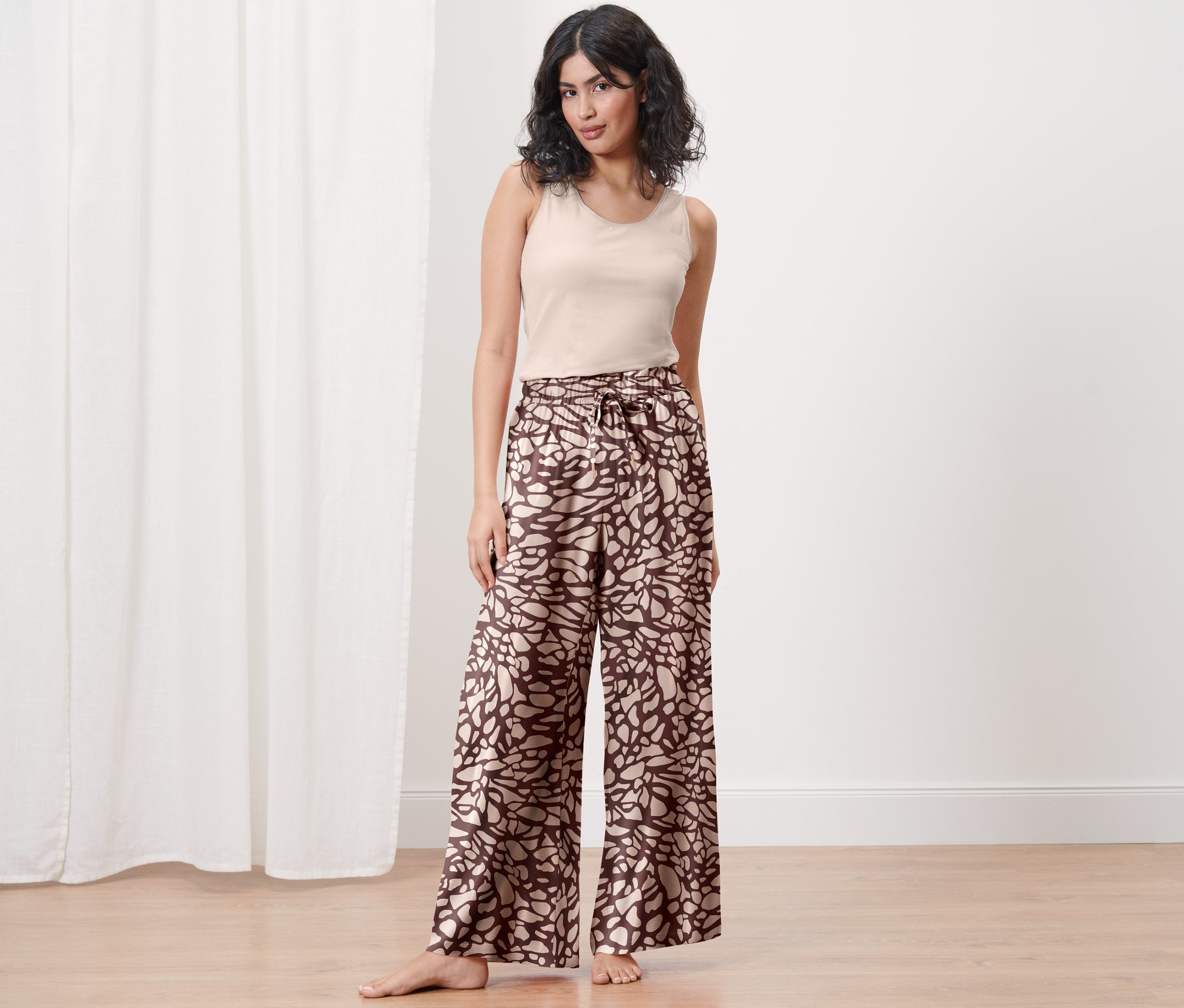 Frau steht barfuß und trägt eine Relaxhose mit Muster und ein Tanktop.