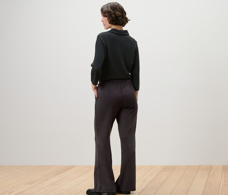 Eine Frau steht mit dem Rücken zur Kamera und trägt eine schwarze Schlupfhose mit Hahnentritt-Jacquard.