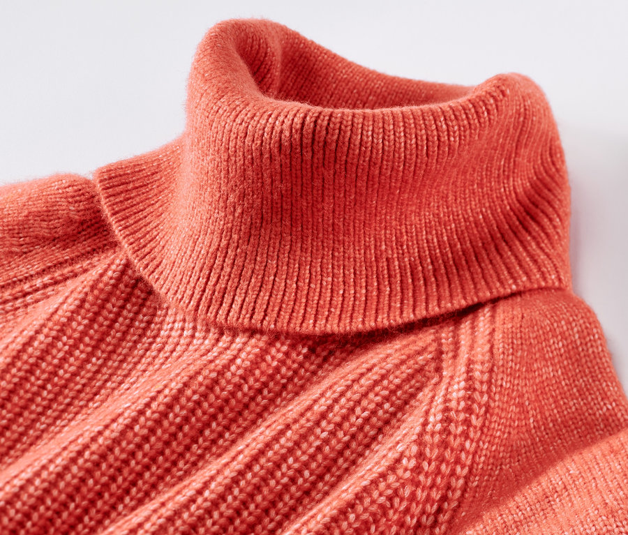 Nahaufnahme eines orangefarbenen Grobstrickpullovers mit Rollkragen.