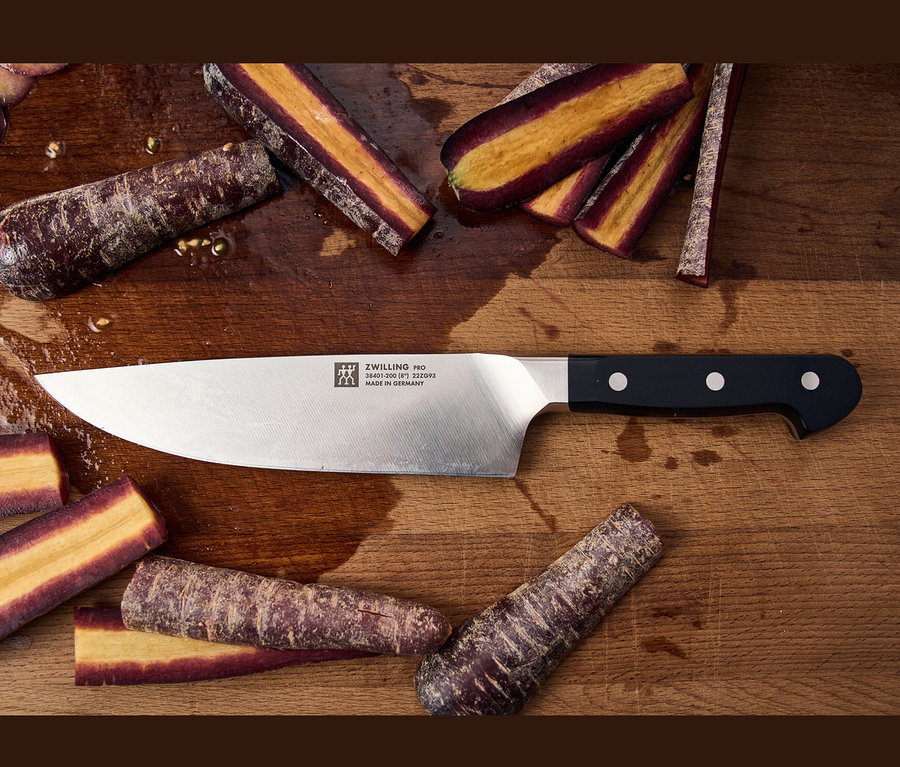 Auf einem Holzbrett liegen ein ZWILLING PRO Messer und geschnittene lila Karotten.