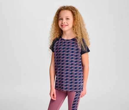 Mädchen mit lockigen Haaren posiert in einem HUMMEL HMLJR Mix T-Shirt S/S und Leggings.