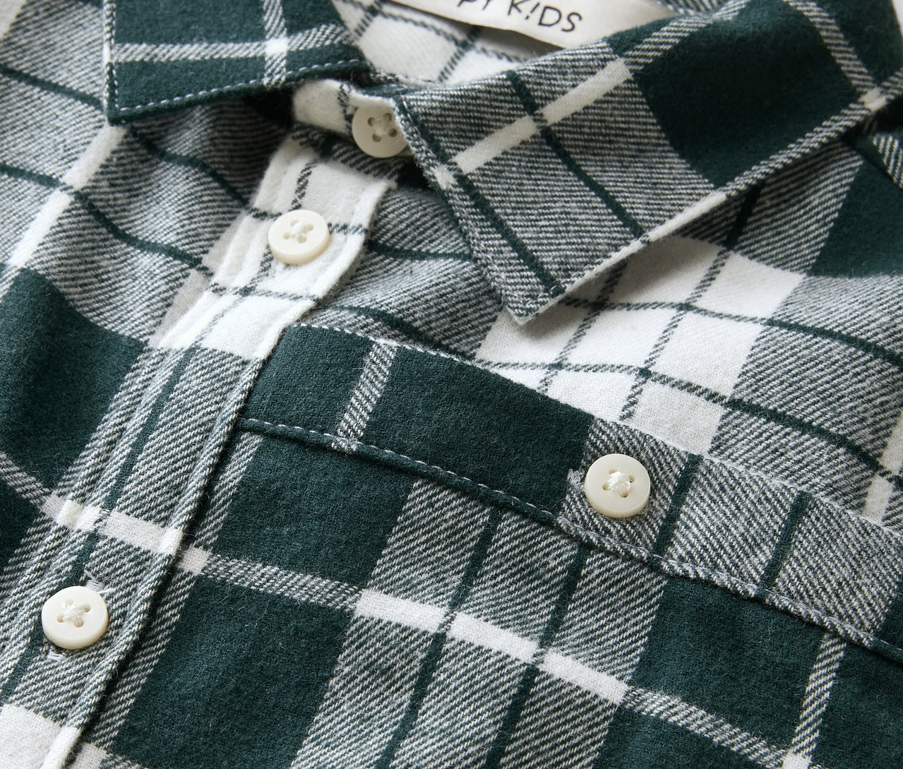 Detail eines grün-weiß karierten Hemdes mit Knöpfen und einem Aufnäher mit der Aufschrift Happy Kids.