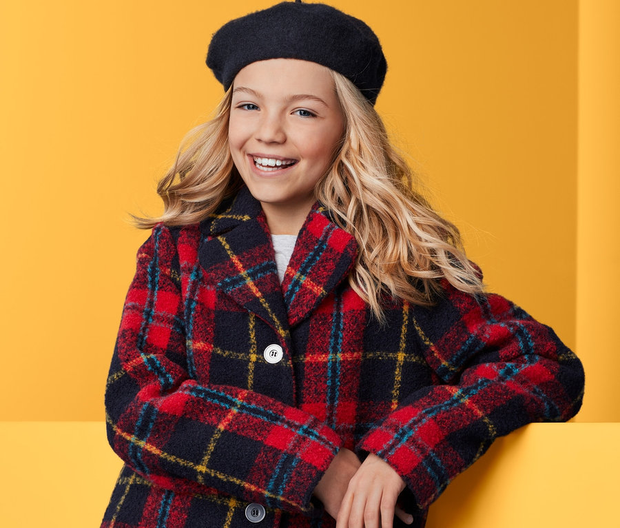Lächelndes Mädchen mit Baskenmütze und kariertem Mantel.
